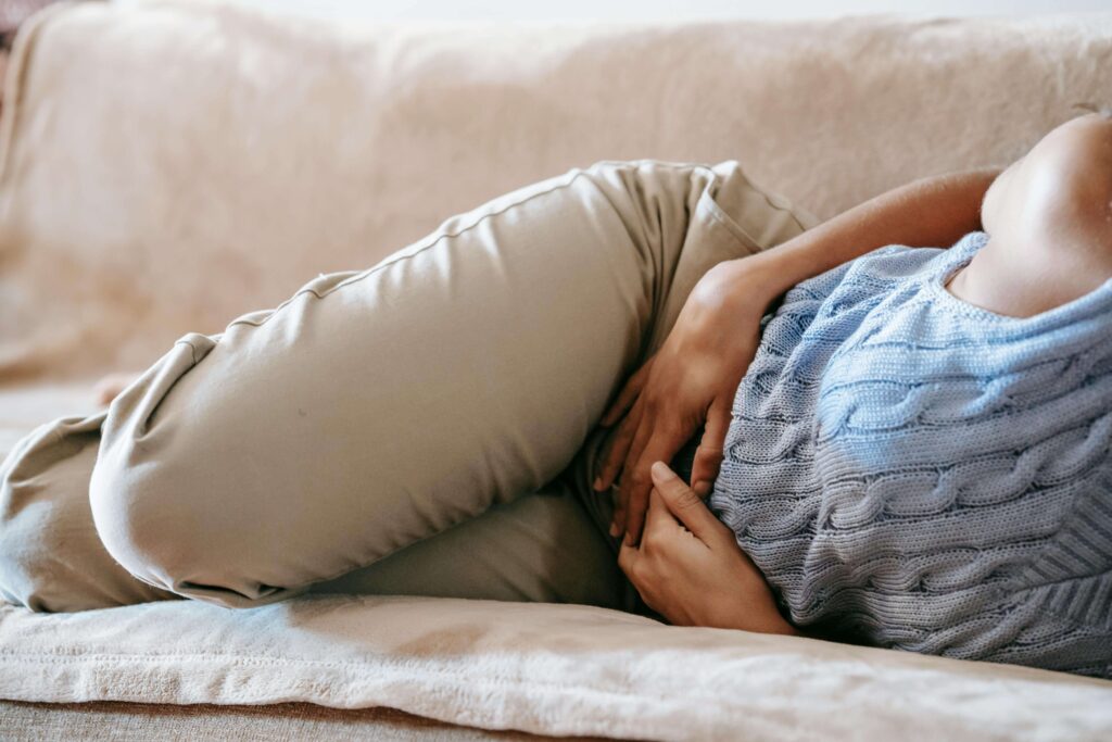 A woman lying on a bed, holding her stomach with a pained expression, possibly experiencing discomfort or cramps
